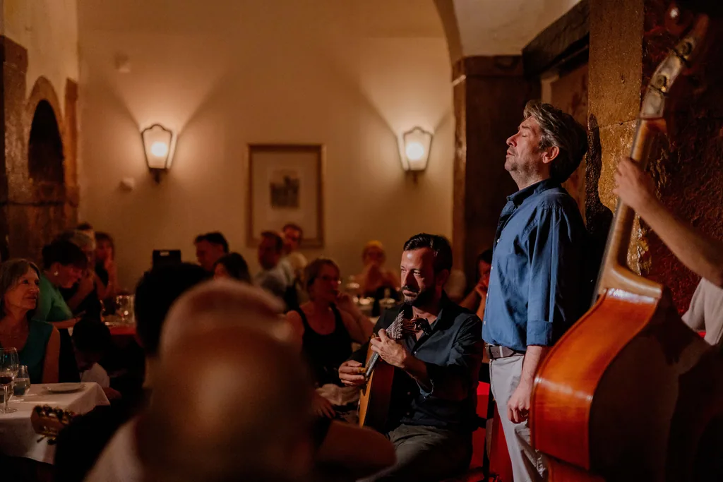 Fadista de olhos fechados, acompanhado à viola de fado e ao contrabaixo, na sala cheia