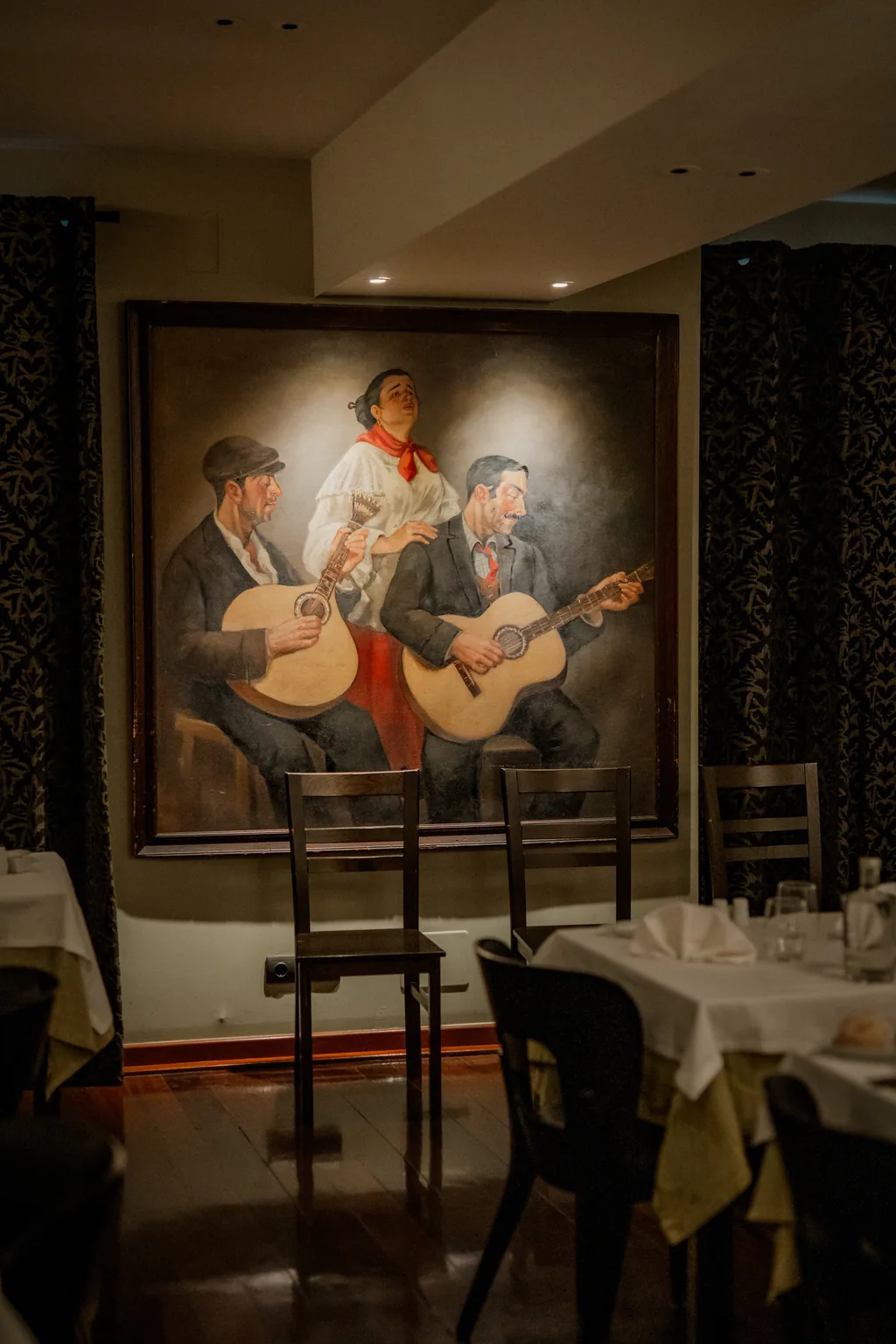A pintura da fadista de lenço vermelho entre os dois guitarristas, sobre as mesas postas