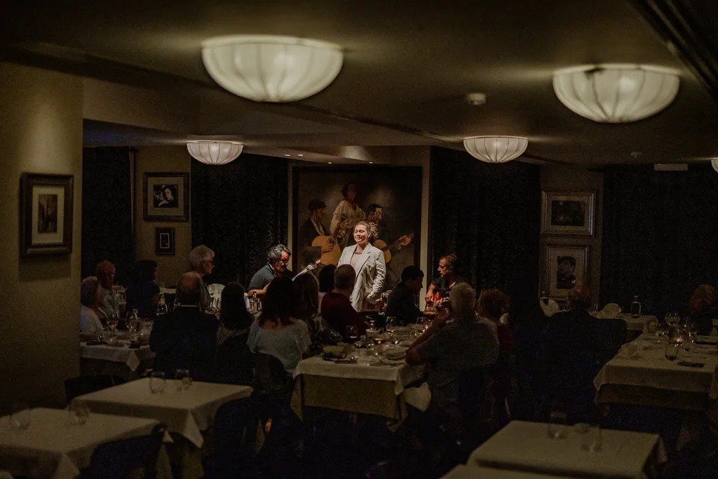 Plano geral da sala cheia durante um fado, com o fadista ao fundo