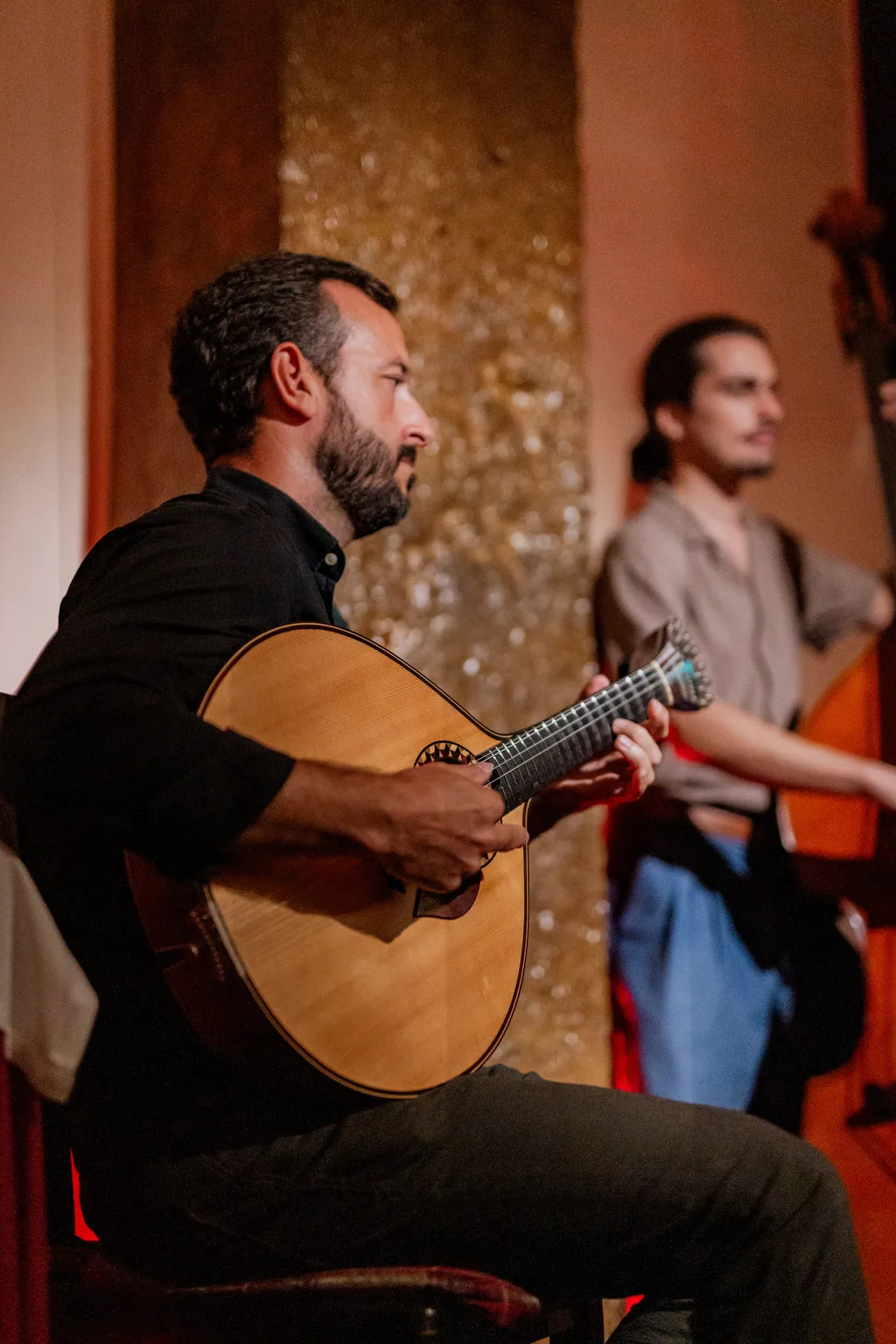 O guitarrista sentado a tocar, o contrabaixista de pé atrás dele