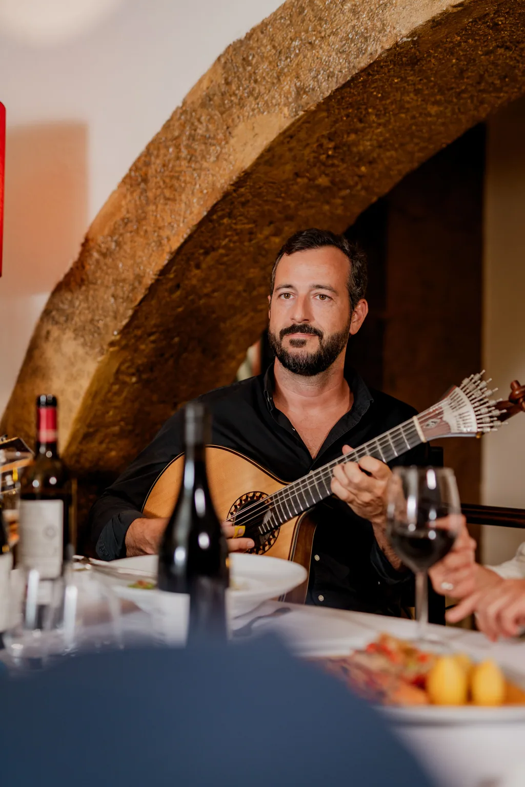Guitarrista sentado à mesa, sob o arco de pedra